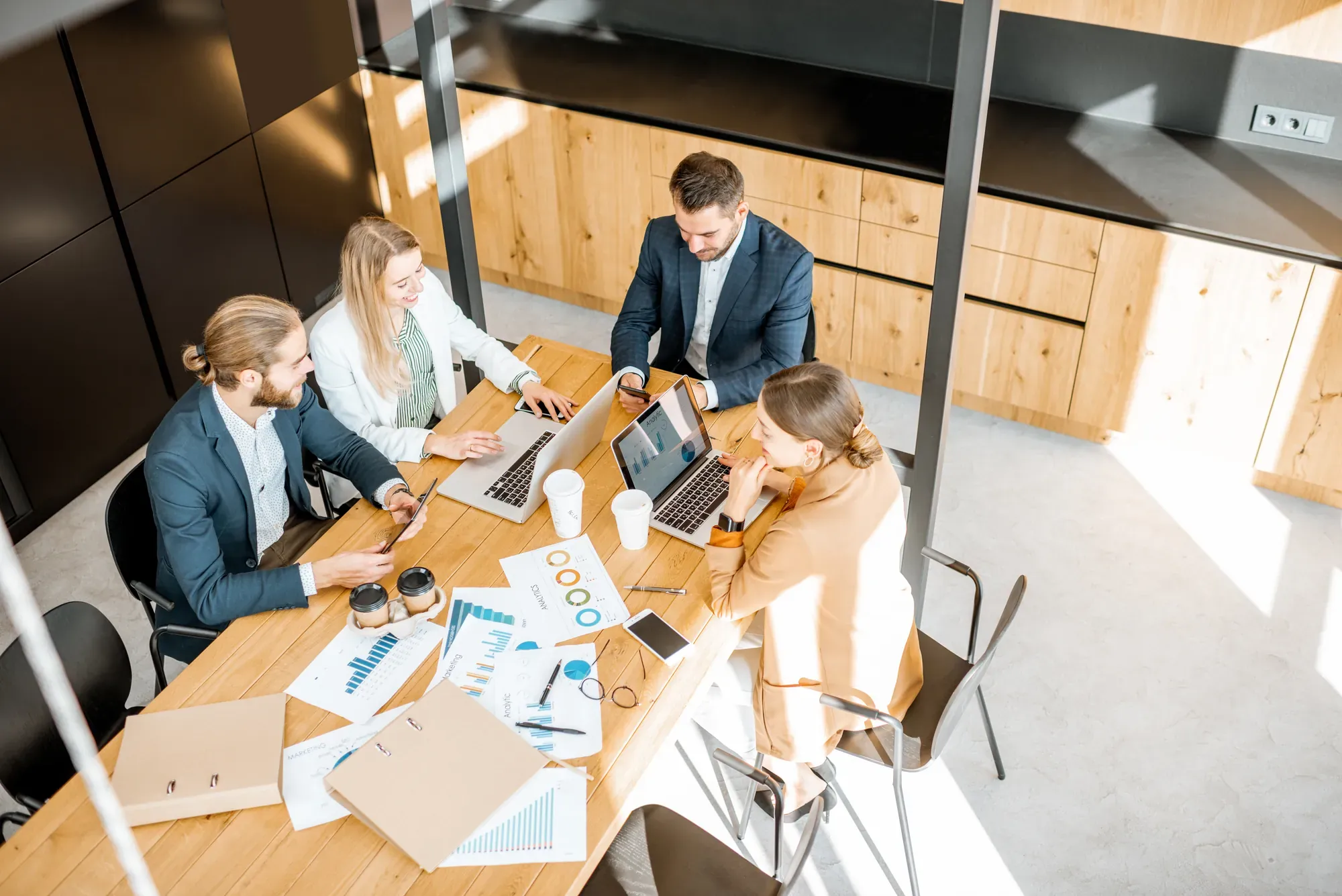 Equipo de trabajo reunido alrededor de una mesa con portátiles y gráficos